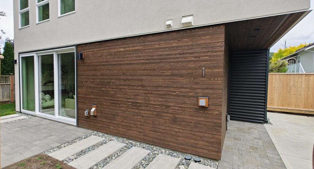 The URBAN NEST siding - Innovate Design Collective Modern home's exterior featuring dark wood cladding, a large glass sliding door, and a light gray upper facade with windows above.